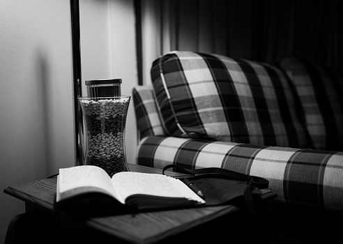 The grayscale view of an opened book and a vase on a small table by the armchair