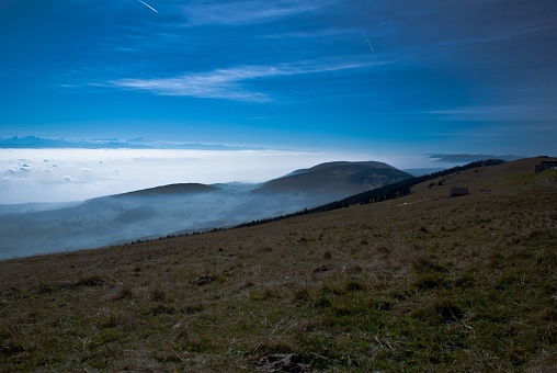 The clouds covering the big mountains under the blue sunny sky with the horizon in the background