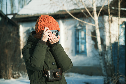 Female tourist is taking pictures with an old film camera (FED 2 which was produced in USSR in 1955-1970) on winter countryside street