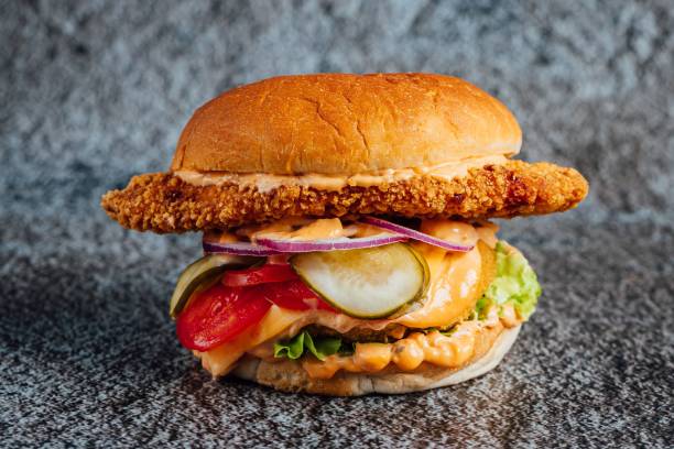 istock Closeup shot of a large fried chicken cheeseburger with vegetables on a gray surface 1453740269
