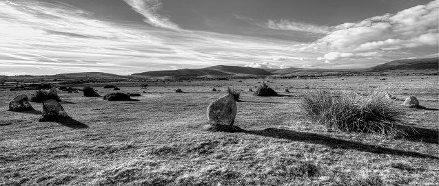 A grayscale shot of Gors Fawr Stone Circle against cloudy sky in daylight in Preseli Hills, Wales, United Kingdom