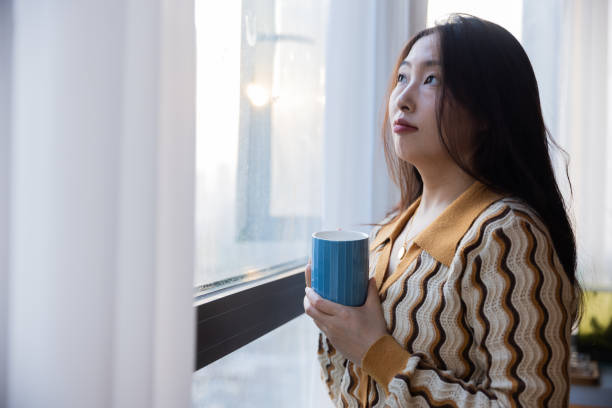 istock Women drinking a cup of coffee standing near window 1453746864