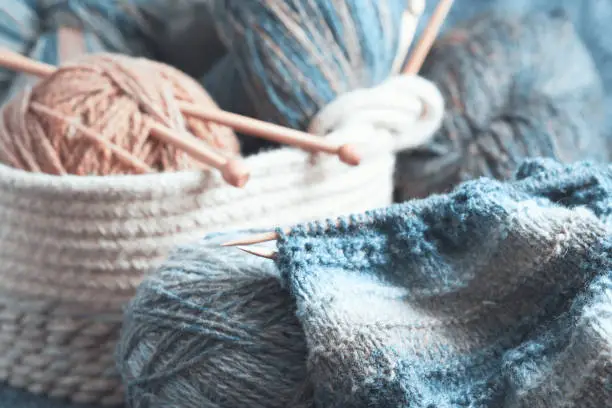 Photo of Knitting in progress. Skeins of wool yarn and wooden knitting needles in a basket.