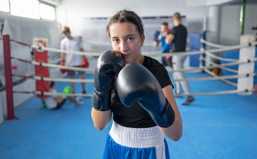Portrait of determined teenage girl boxer in a fighting stance on sports training in a gym. Combat sport and Kids sport concept.