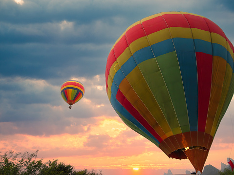 View of colourful hot air balloon in preparation for flight in foreground, against beautiful sky with sun in horizon
