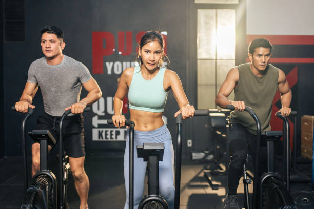 gruppo di giovani atleti che fanno esercizio insieme in palestra fitness. attraenti esercizi di allenamento per sportivi attivi e donne insieme pedalando su una macchina da bici per la salute e il benessere nello stadio. - spinning health club instructor gym foto e immagini stock