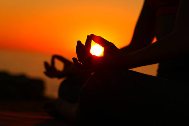 Carefree female athlete doing Yoga relaxation exercises wit her hands clasped on a cliff above the sea at sunset. Copy space.
