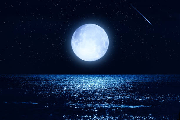 istock Full Moon with starry skies rising above ocean horizon. 1453754729
