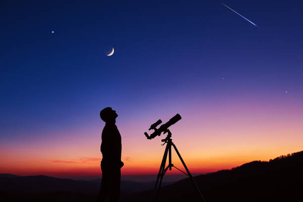 Man with astronomy telescope looking at the night sky, stars, planets, Moon and shooting stars. stock photo