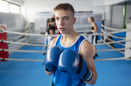 Portrait of determined teenage boy boxer in a fighting stance on sports training in a gym. Combat sport and Kids sport concept.