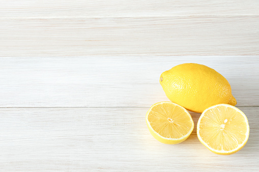 Whole and cut ripe lemons on a white wooden background. Copy space for text