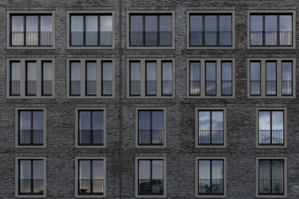 a fragment of the facade of a building with windows. Facing with black brick. Two- and three-leaf windows on a gray brick facade. Architectural background. Multi-storey residential building