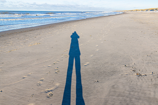 Image of a long shadow of a person on a wide sandy beach in the evening