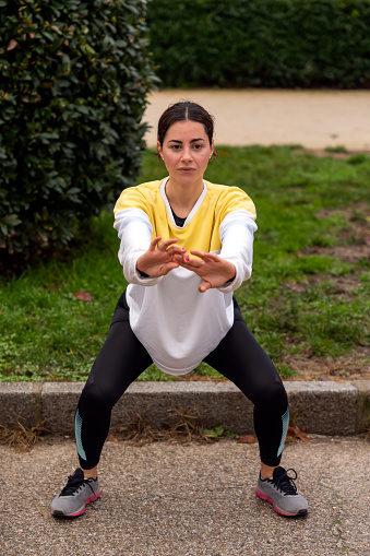 From above full body of young female athlete in sportswear doing squats in park