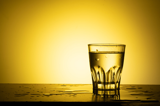 Water glass on table against yellow light, drinking glass