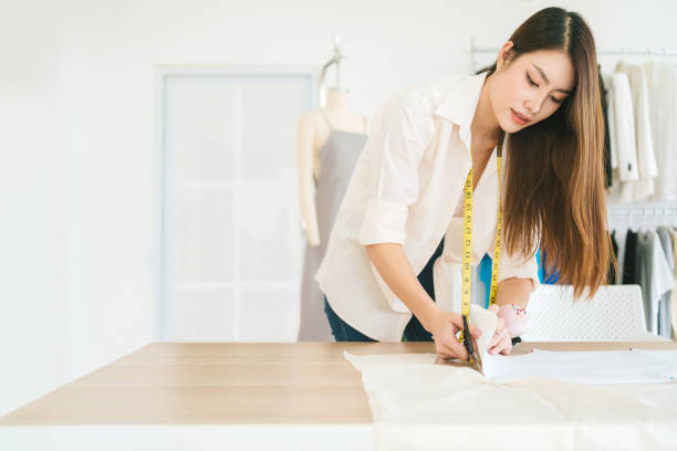istock Asian fashion designer or tailor cutting fabric with scissors for making a pattern of clothes. Fashion designer tailor or sewer in the workshop working for new collection clothes. 1453762455