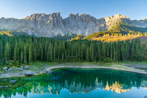 Italian alps in sunrise. Silent morning on the lake of Carezza surrounded by pine forest and mountains.