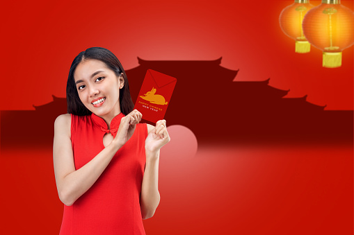 Asian Chinese woman in a cheongsam dress holding red envelopes with a rabbit symbol. Happy Chinese New Year. Chinese New Year of Rabbit
