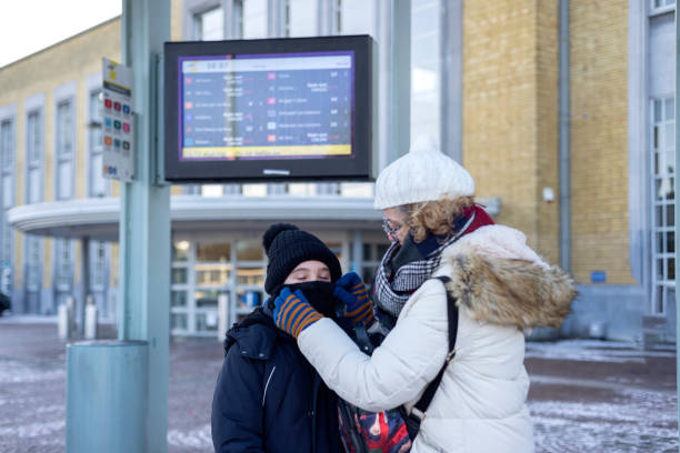 una donna adulta mette una sciarpa calda su suo figlio alla fermata dell'autobus in una fredda giornata invernale. - bus family travel destinations women foto e immagini stock