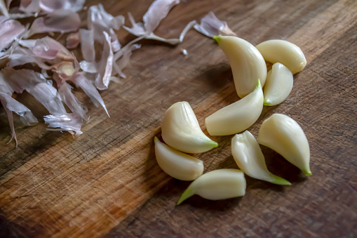 Cloves of garlic sprouted without husks on a wooden table. Peeled garlic on a wooden board next to the husk. Peeled garlic.