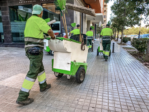 Valencia, Spain - October 2, 2022: Group of street sweepers walking in the street with their equipment. Everyday hundreds of them work everywhere in the city to keep it as clean as it looks