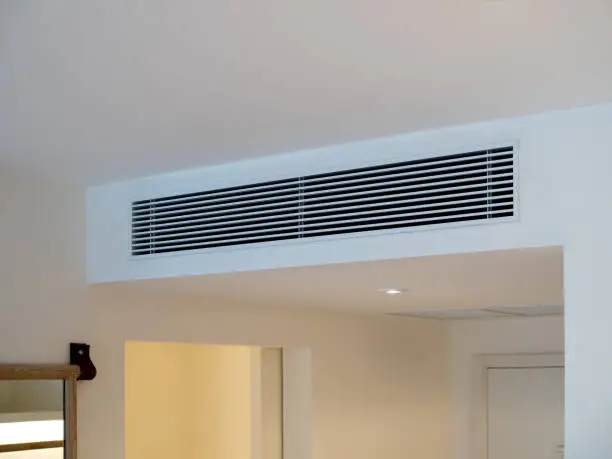 Photo of Air conditioning wall mounted ventilation system on ceiling in the white hotel room. Hotel room air ventilation grill on the wall.