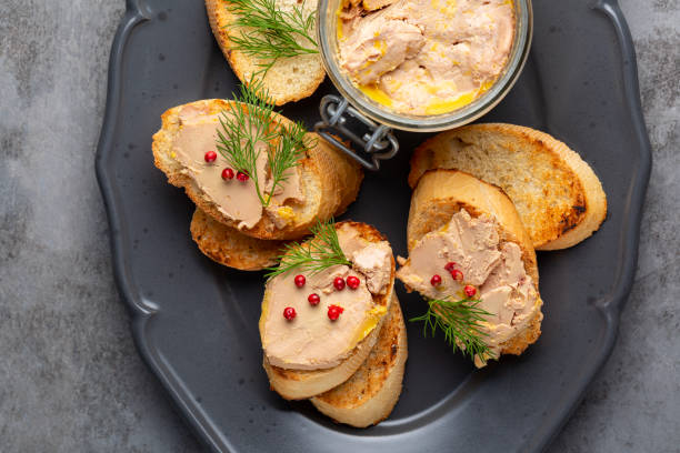 Bread or baguette toast with foie gras pate, directly above. A specialty food product made of the liver of a duck or goose,  in a glass jar. Decorated with red pepper and dill. stock photo