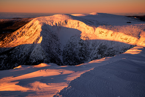 Panoramic view at sunrise of man at the summit looking out at dramatic landscape of snow covered mountains and glacial lakes, shot in New Zealand.