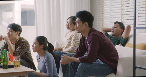 若い大人の友人のグループ 男女 アジアの人々はソファに座る ソファ ソファ ジョイ ナイト パーティー 楽しい ゲーム 自宅でテレビの生放送 食べる スナックボウル 飲み物 ビール瓶 ガラス  - ワールドカップ　日本人 ストックフォトと画像
