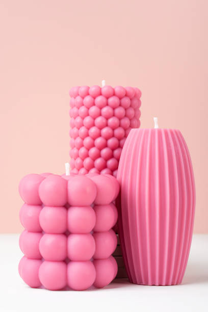 Handmade olive wax different forms pink color candle on a duotone pastel pink and white background. Sustainability vegan candle, natural materials. Minimalistic, modern photo. Copy space. vertical.