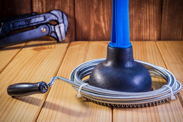 Clean plastic plunger with blue handle, pipe wrench and cable on wooden background.. Plumbing tools for sewer cleaning