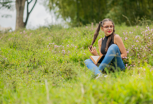 Young woman outdoors in her favorite hobbies, reading, enjoying and playing guitar.