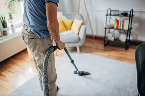 Young woman using a vacuum cleaner while cleaning carpet in the house.