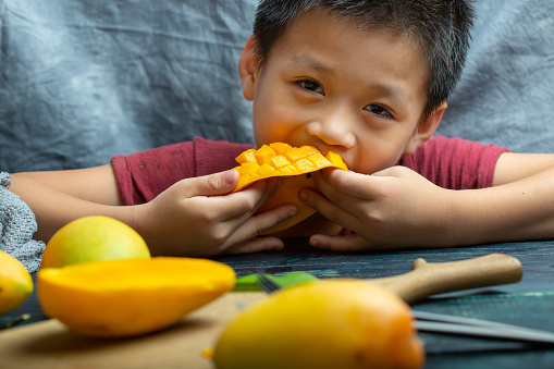 A cute little boy eats mango at home