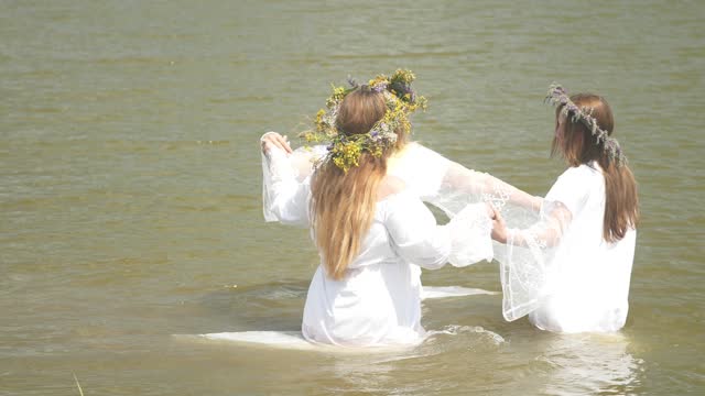 Historical reconstruction of the Feast of Ivan Kupala. Opening of the swimming season. Women in white dresses and wreaths dance in the lake in the rays of the bright sun