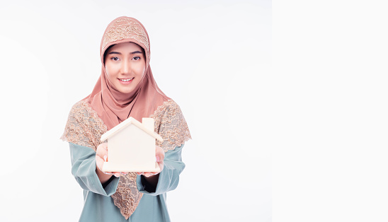 Muslim woman holding small house model Muslim girl isolated on white background in studio Saving Banking Loan concept copy space Showing wooden house model Use for Advertising Banking Financial