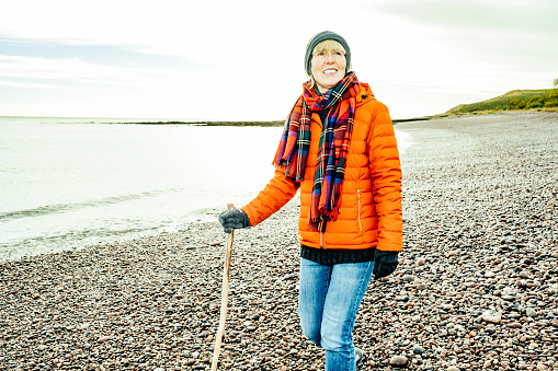 Woman walking on the pebble beach with a wooden stick at Inverbervie on the east coast of Aberdeenshire, Scotland.