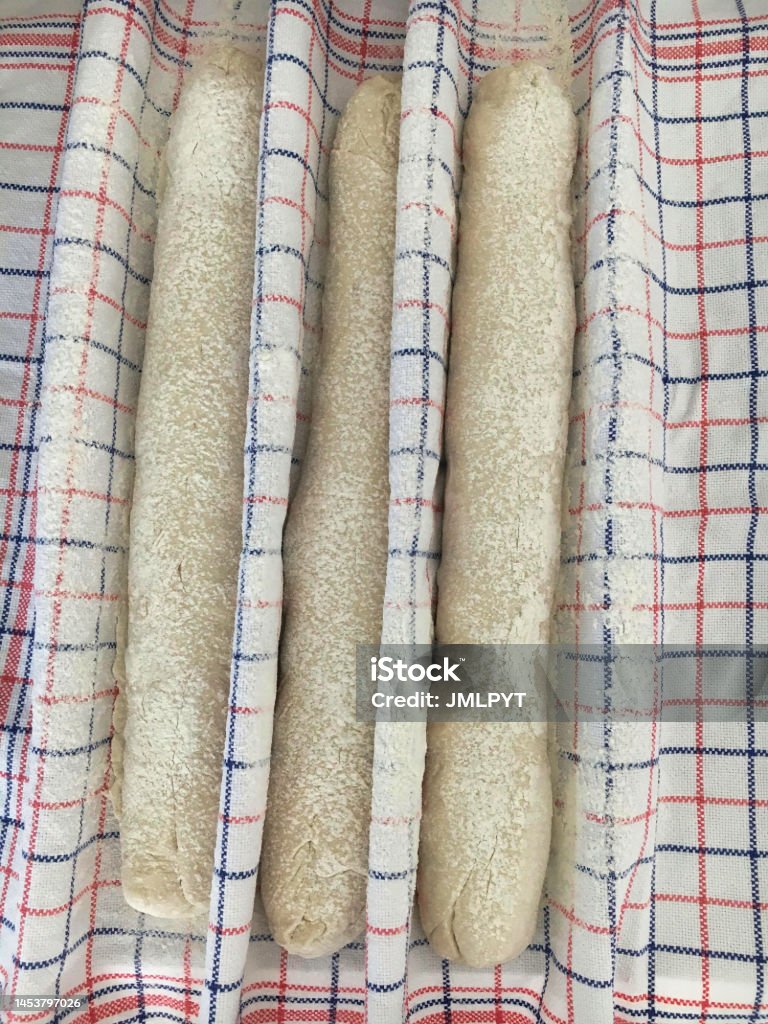 Baguette ready to bake High angle view of three raw baguettes of bread, lying on a blue and red checkered tea towel, with flour on them, ready to be baked. Baguette Stock Photo