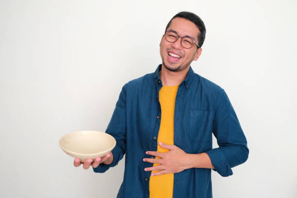 istock Adult Asian man showing empty bowl with happy expression while touching his stomach 1453797947