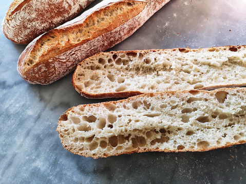 bird's eye view of three loaves of bread, one of which is cut in half and allows you to see the crumb of bread.