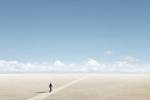 Woman On A Long Walk Toward The Horizon A lone woman takes a long walk on a path toward the horizon on a sunny day across a barren desert floor. horizon over land stock pictures, royalty-free photos & images