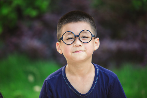 The smiling face of a little boy with glasses in the park