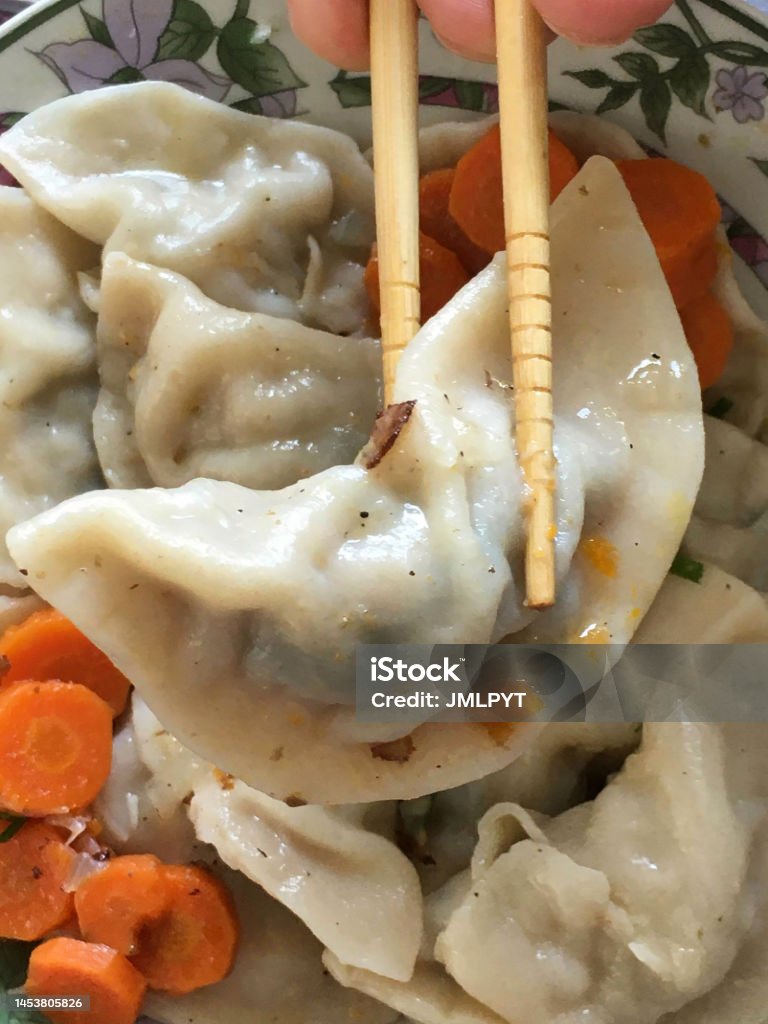 Chinese traditional dumplings Chinese dumplings in a plate with chopped carrots and chopsticks grabbing a dumpling. Close up. Appetizer Stock Photo