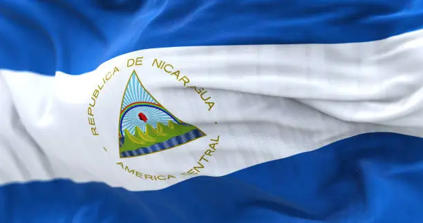 Close-up view of the Nicaragua national flag waving. It is blue, white, and blue with a national coat of arms and. Fabric textured background. Selective focus. Realistic 3d illustration