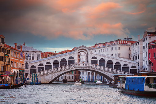 Famous Rialto bridge, early in the morning, with traditional gondolas, passenger transport boat (vaporettos) and cargo boat, on the Grand Canal in Venice, Italy