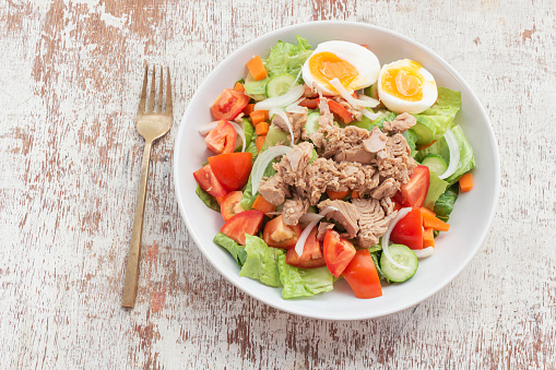 Tuna salad add egg in white bowl isolated on wood background close up, top view, healthy food concept.