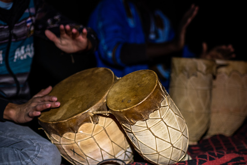 Merzouga, Morocco; 11th december 2022: Detail of the hands and drums of several people playing percussion instruments at night. During the camps organized for tourists to spend the night in the desert it is common for locals to perform percussion performances.
