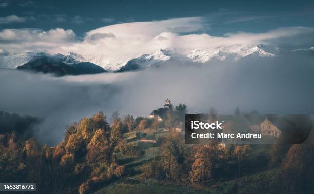 French Mountain Village Emerging From The Fog With The Snowy Mountain In The Background Stock Photo - Download Image Now