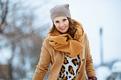 smiling stylish female in brown hat and scarf in camel coat