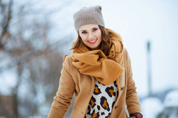 smiling stylish female in brown hat and scarf in camel coat stock photo